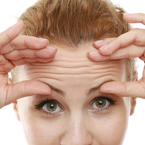 Woman touching forehead wrinkles in mirror.