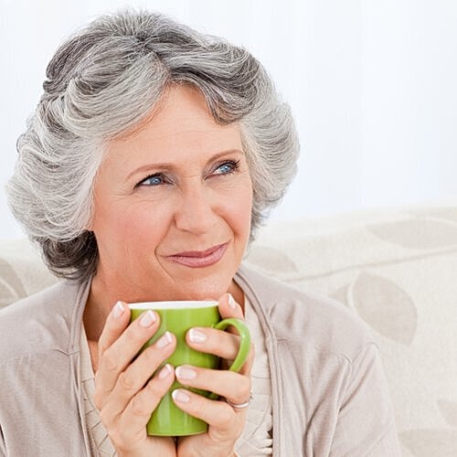 Woman in her 60s smiling while holding a coffee cup