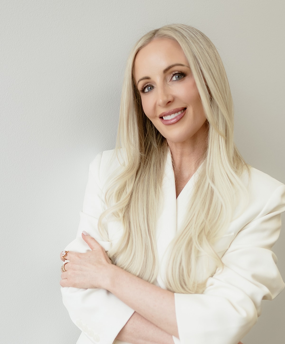 Smiling woman in a white blazer, arms crossed.
