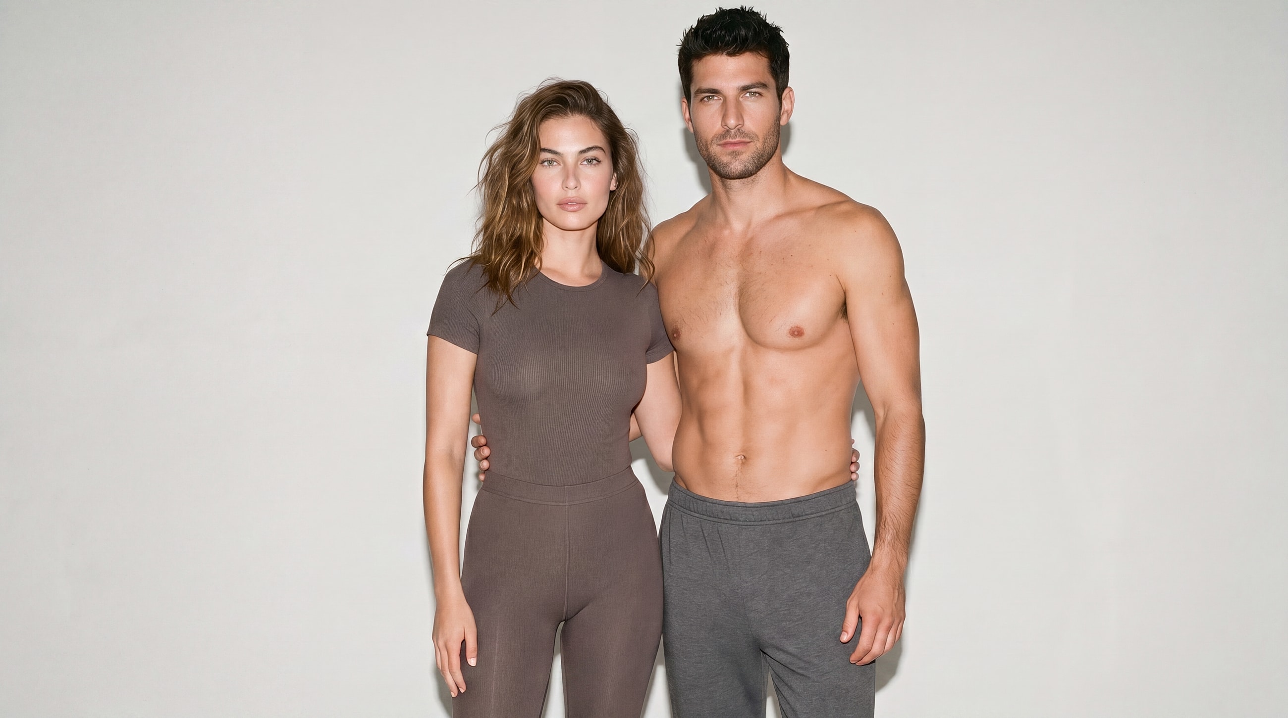 Couple in matching fitted clothing against neutral background.