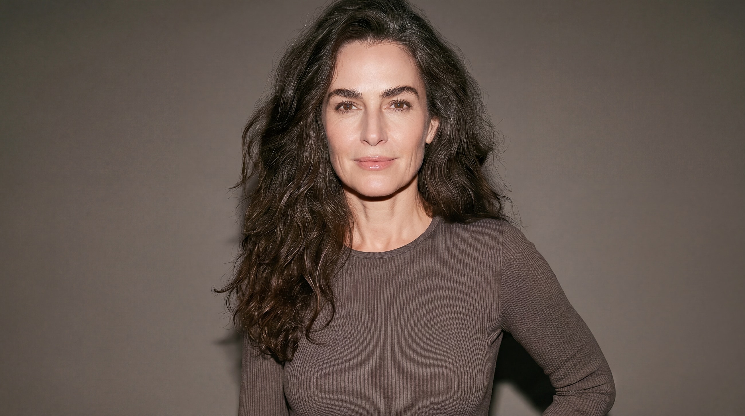 Woman with long, dark hair, smiling confidently.