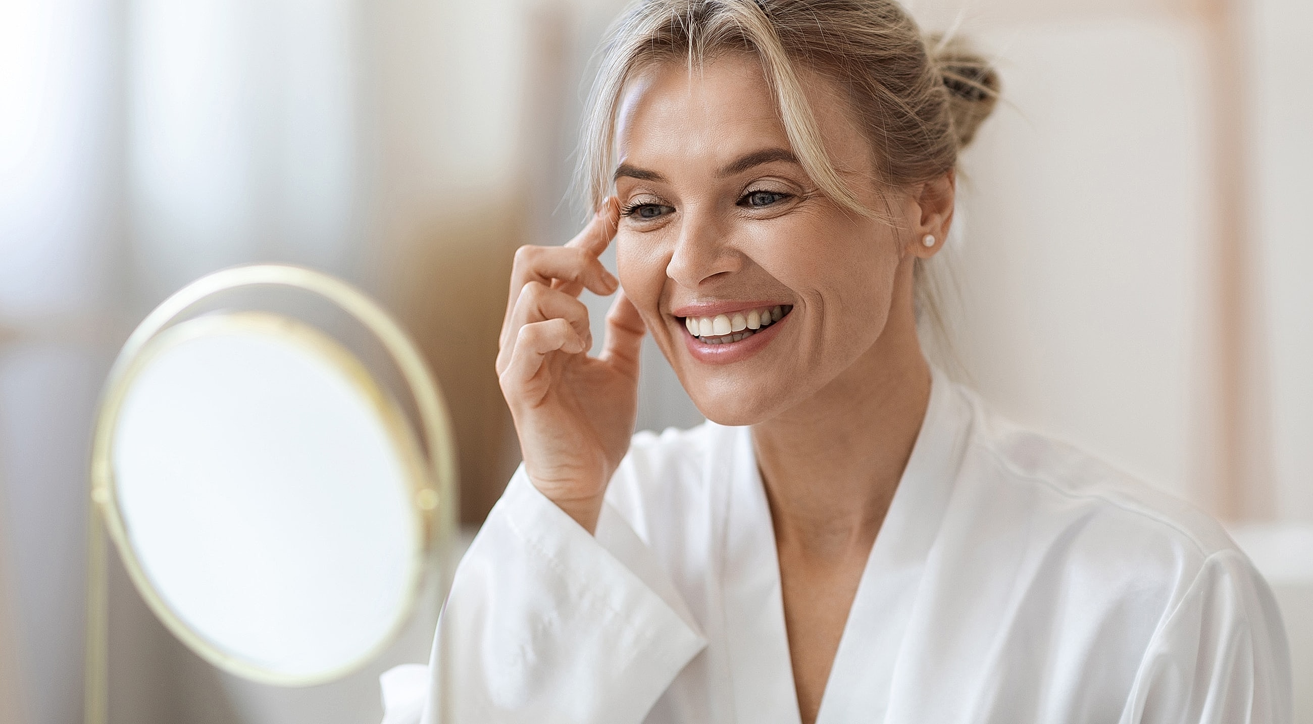 Woman applying skincare, smiling at mirror.