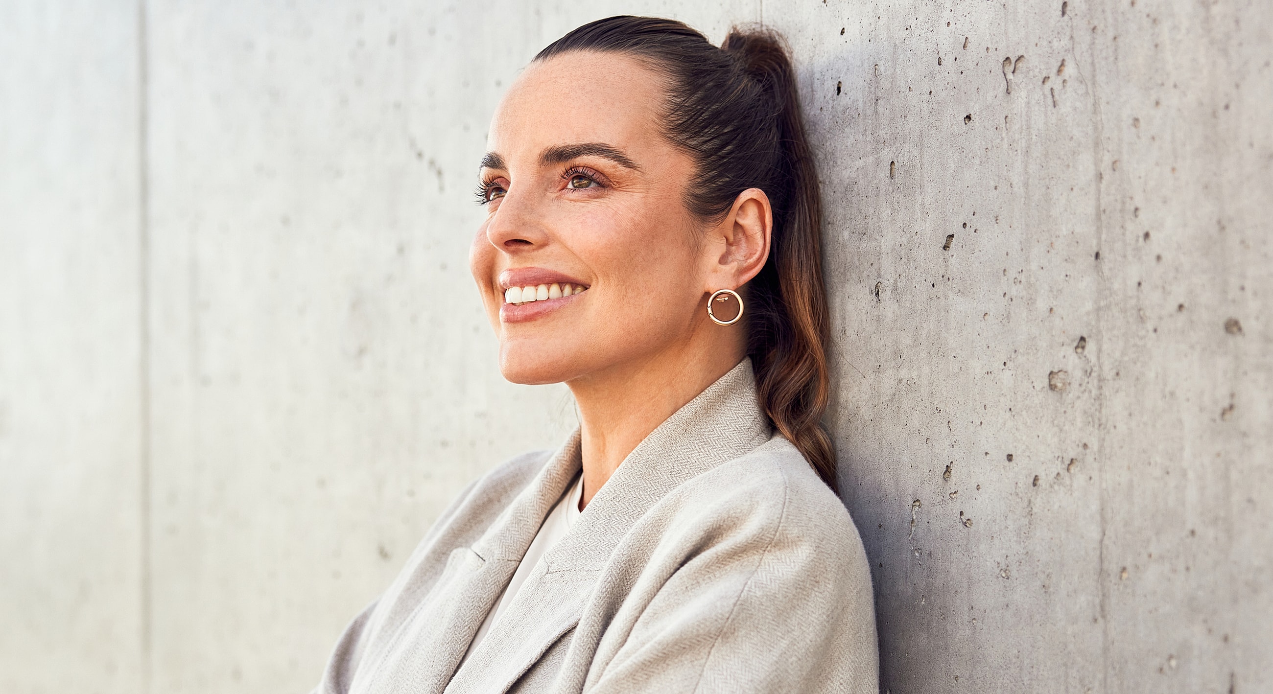 Smiling woman leaning against a textured wall.