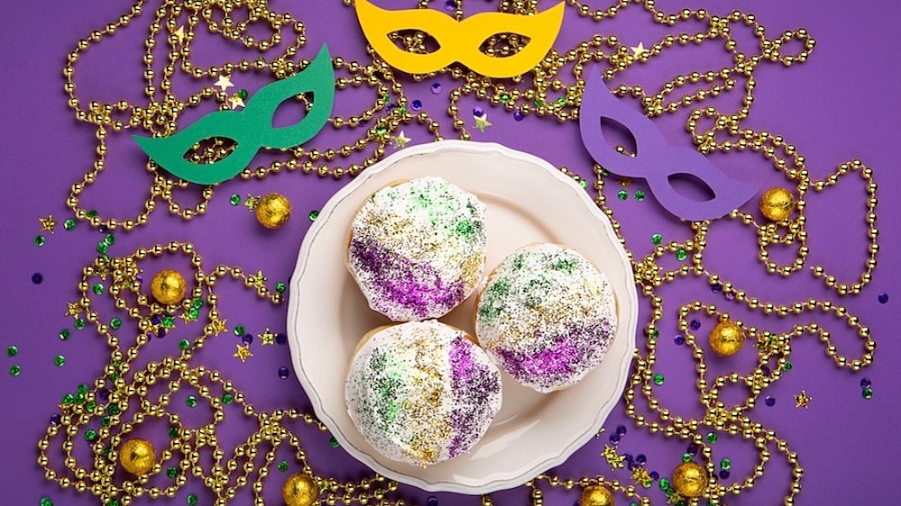 A plate of donuts on a purple background, surrounded by mardi gras masks and beads