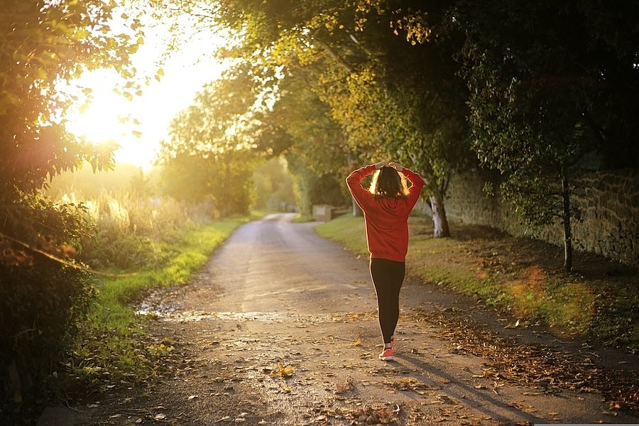 A person in an orange jacket walking down a tree-lined road at sunset