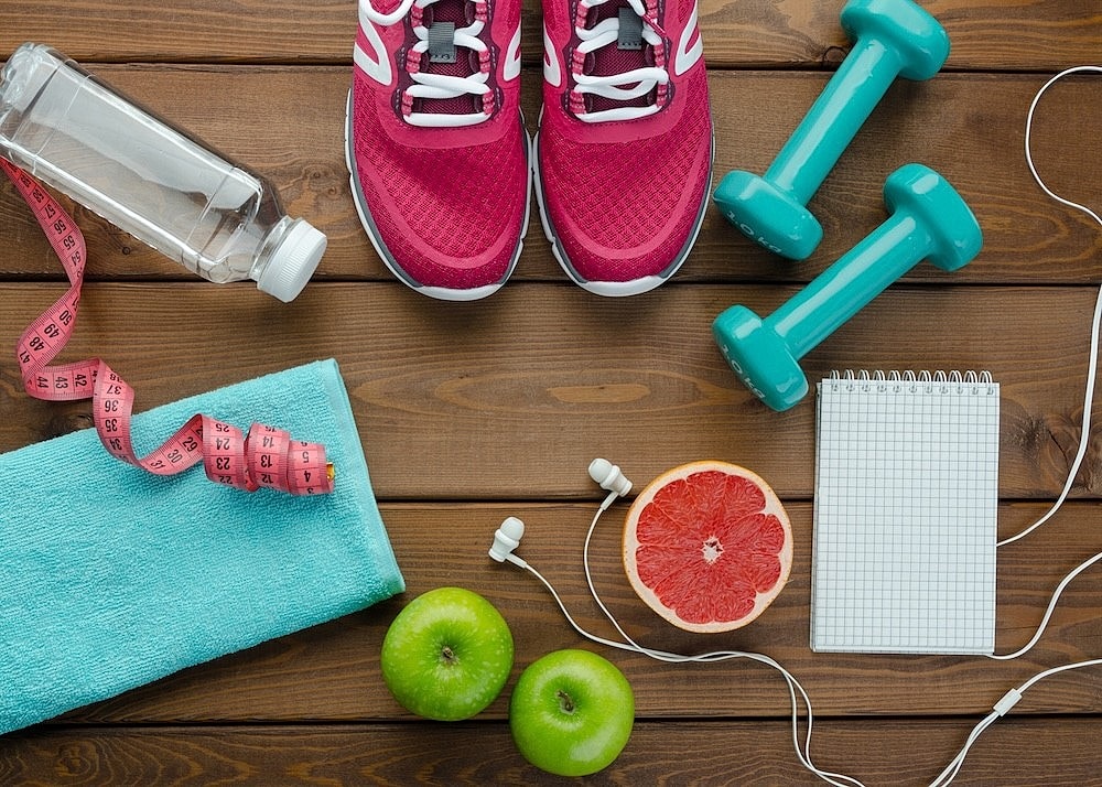 A selection of food and workout accessories spread out in a circle on a wooden floor