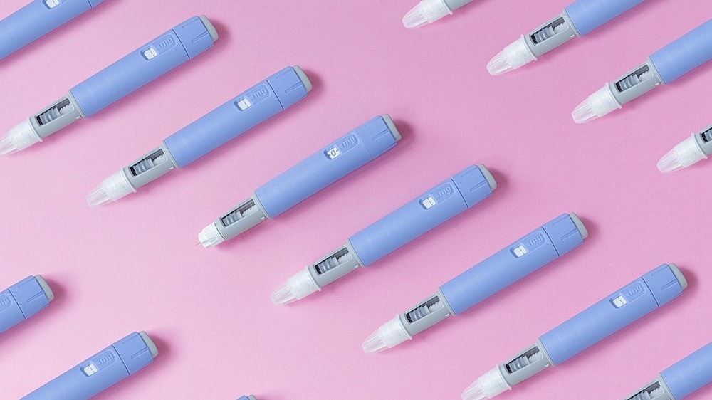 Several light blue medication injectors arranged on a pink background