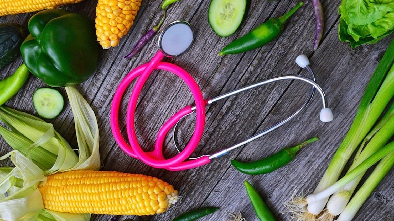 A pink stethoscope surrounded by vegetables