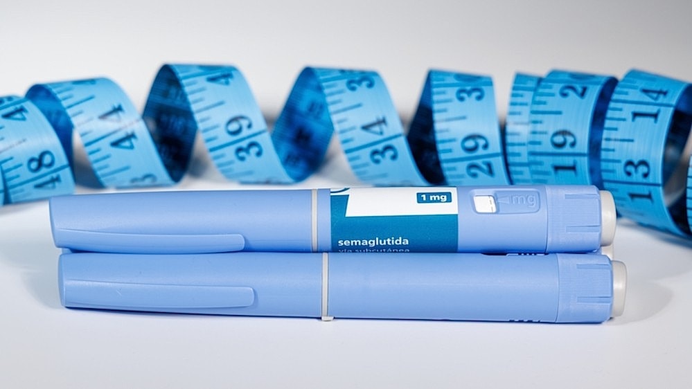 Two light blue semaglutide injectable pens with a curled tape measure in the background