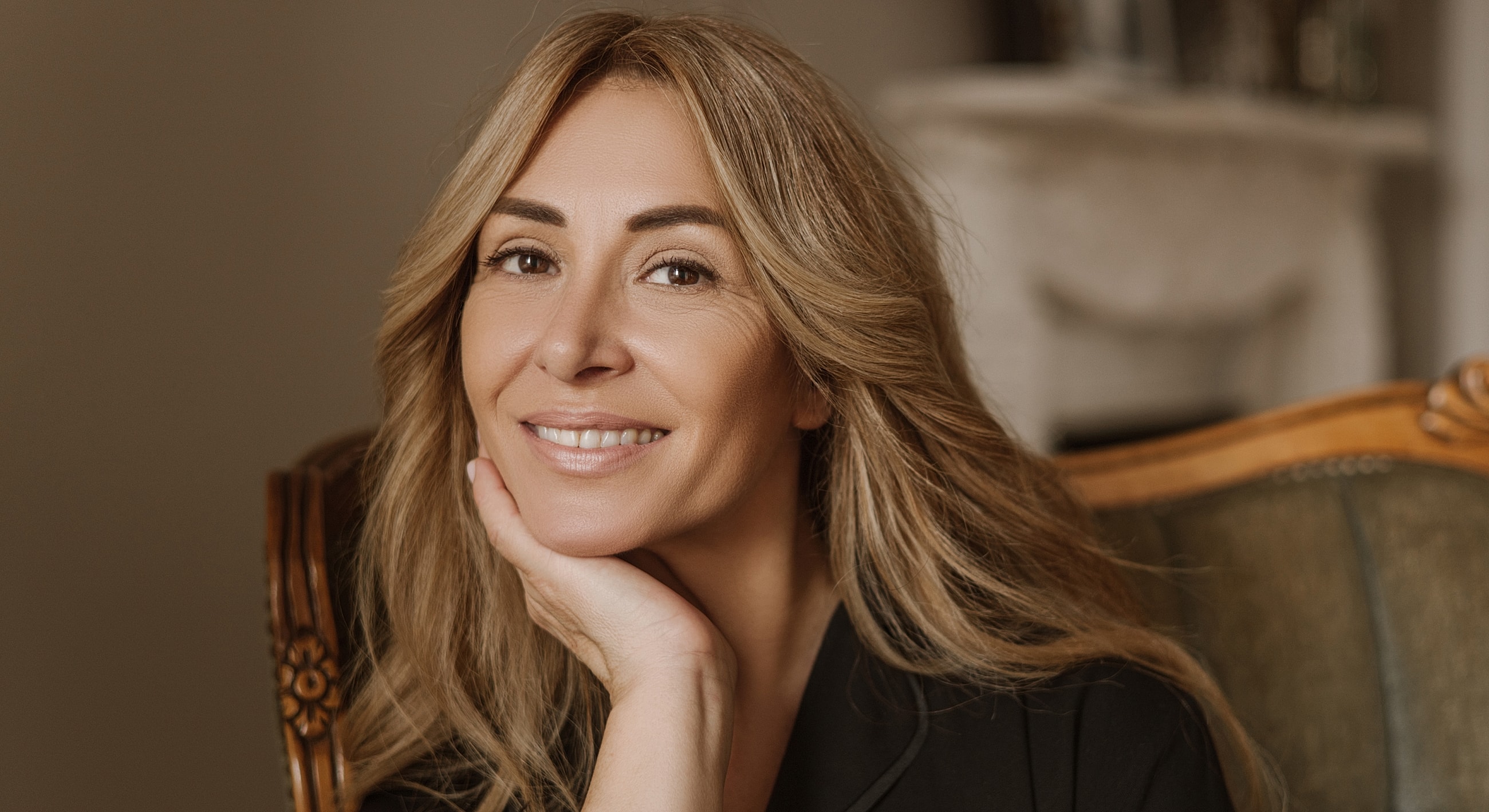 Woman smiling with hand on chin in cozy setting