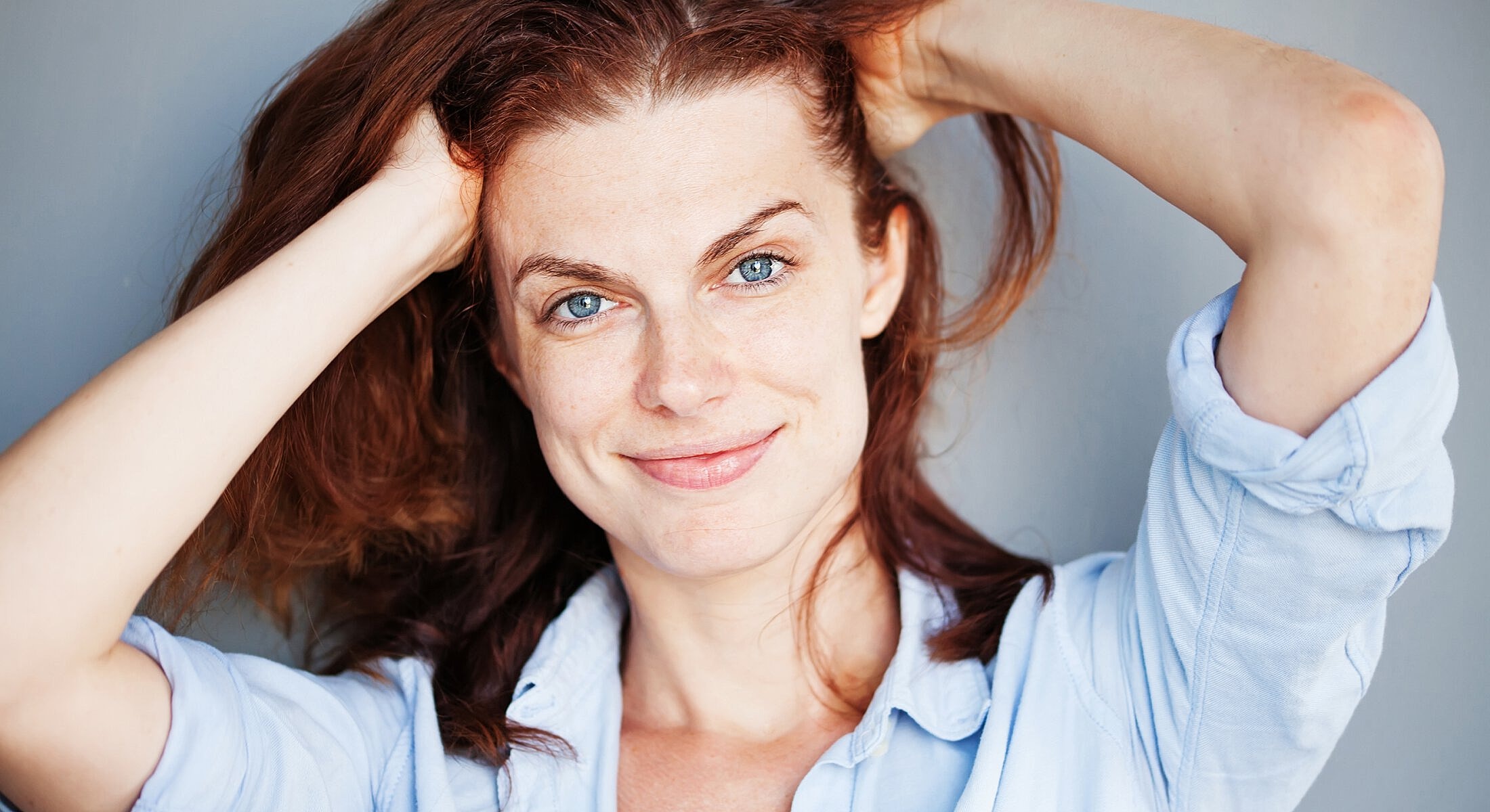 Smiling woman with tousled hair against gray background.