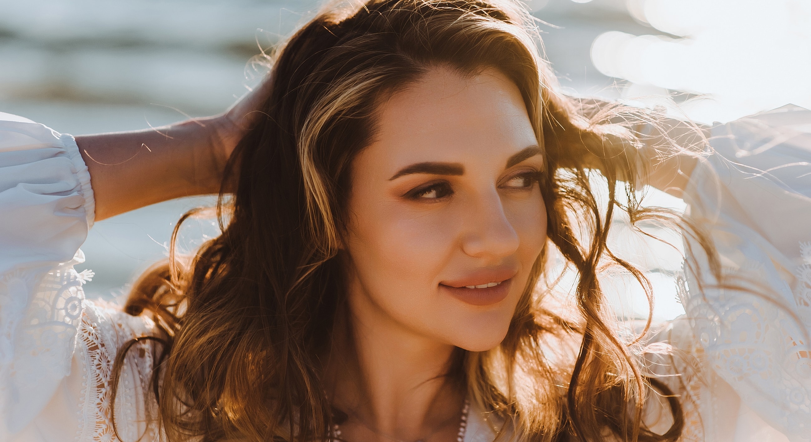 Woman with wavy hair by water, enjoying sunlight.