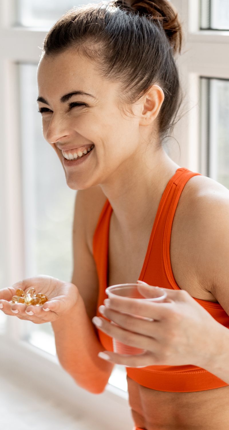 Woman smiling with supplements and drink in hand.