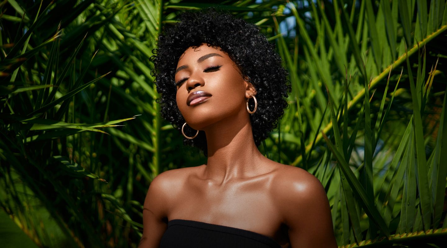 Woman with curly hair in a lush setting.