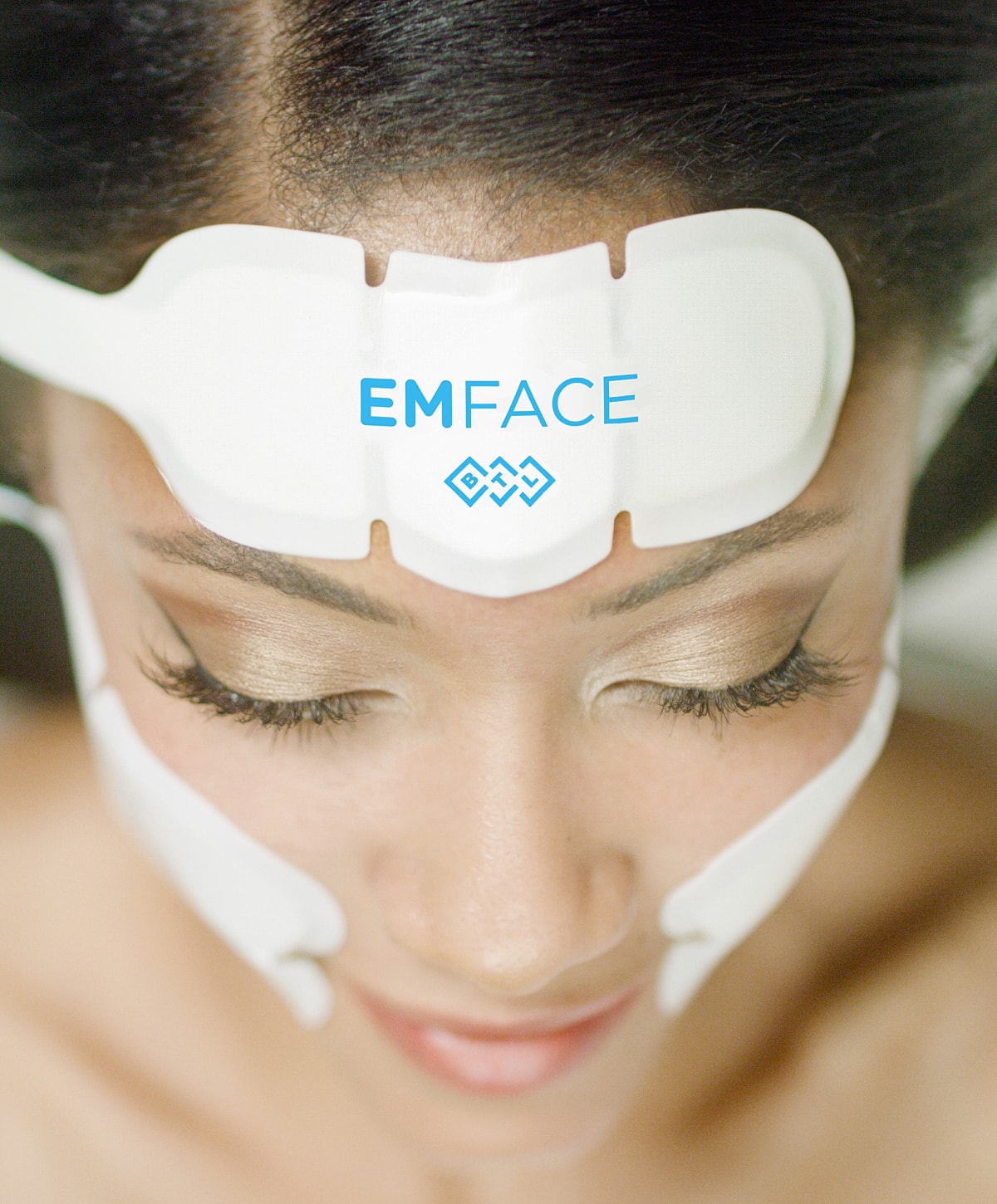 Woman using EMFACE device for facial treatment.