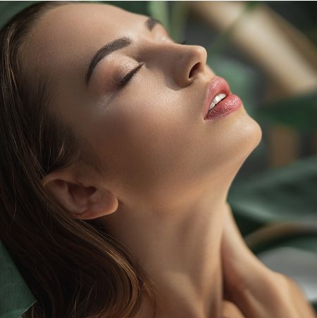 Woman with closed eyes amidst green foliage.