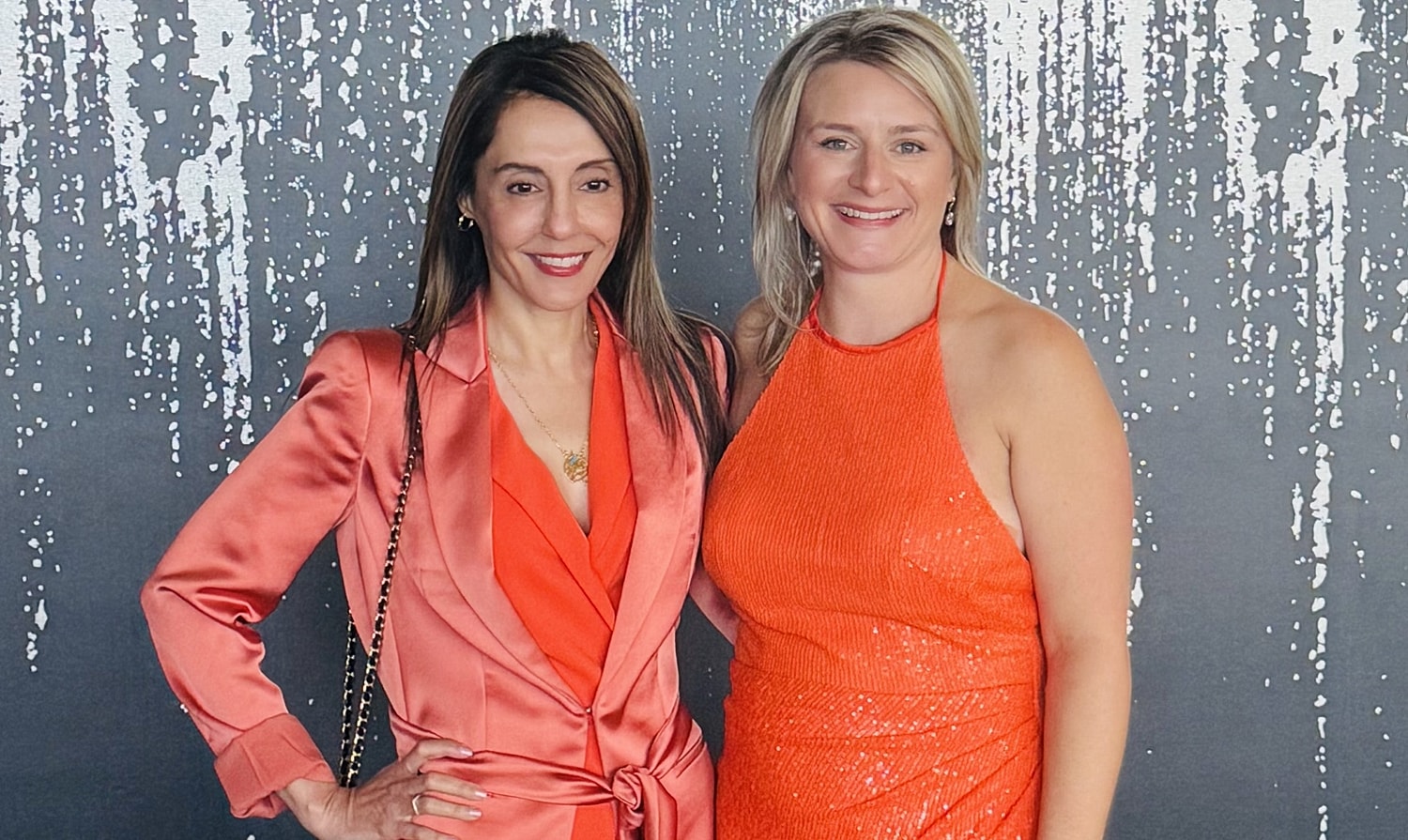 Two women in orange outfits posing together.