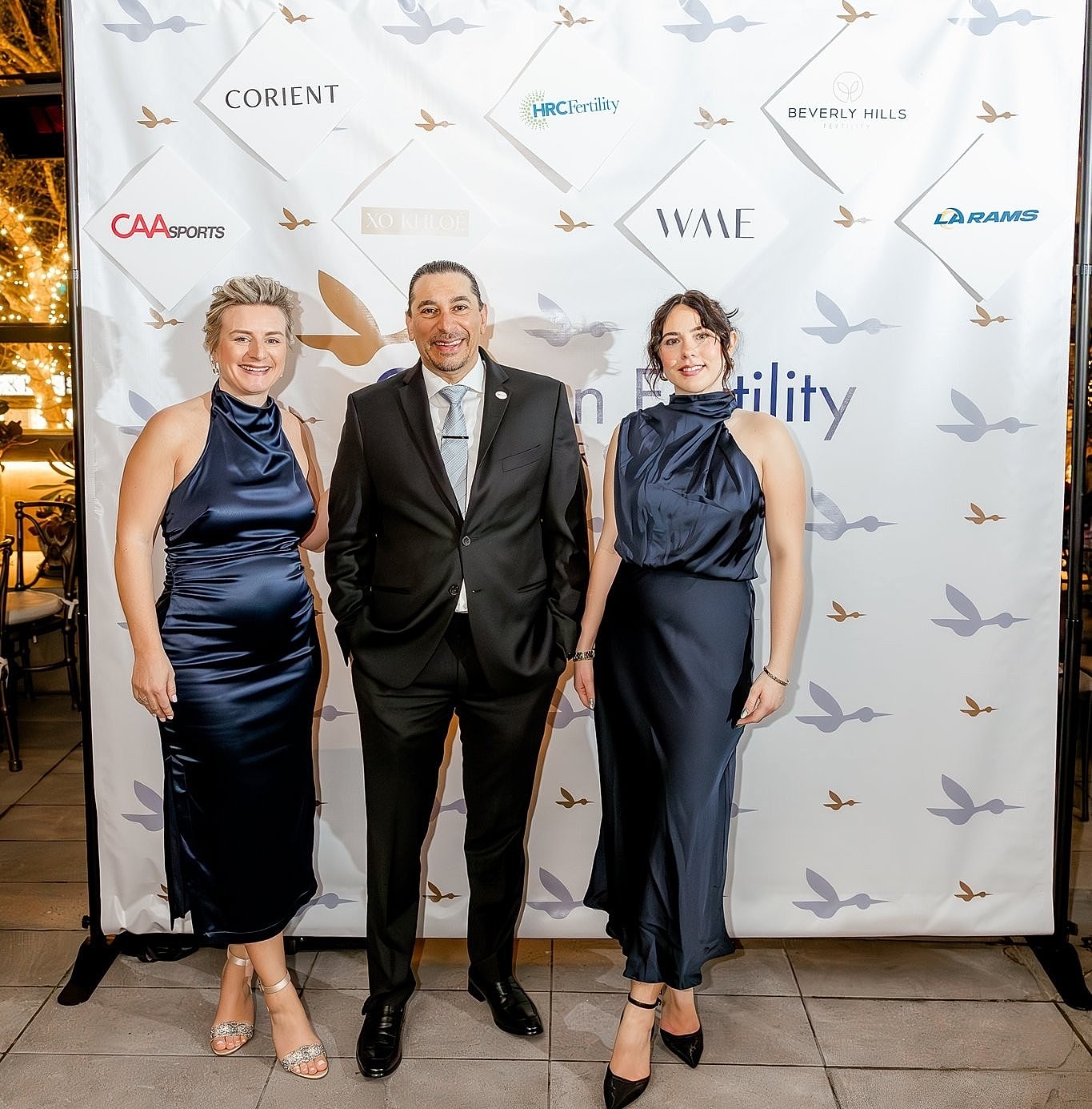 Three attendees at a formal event backdrop.
