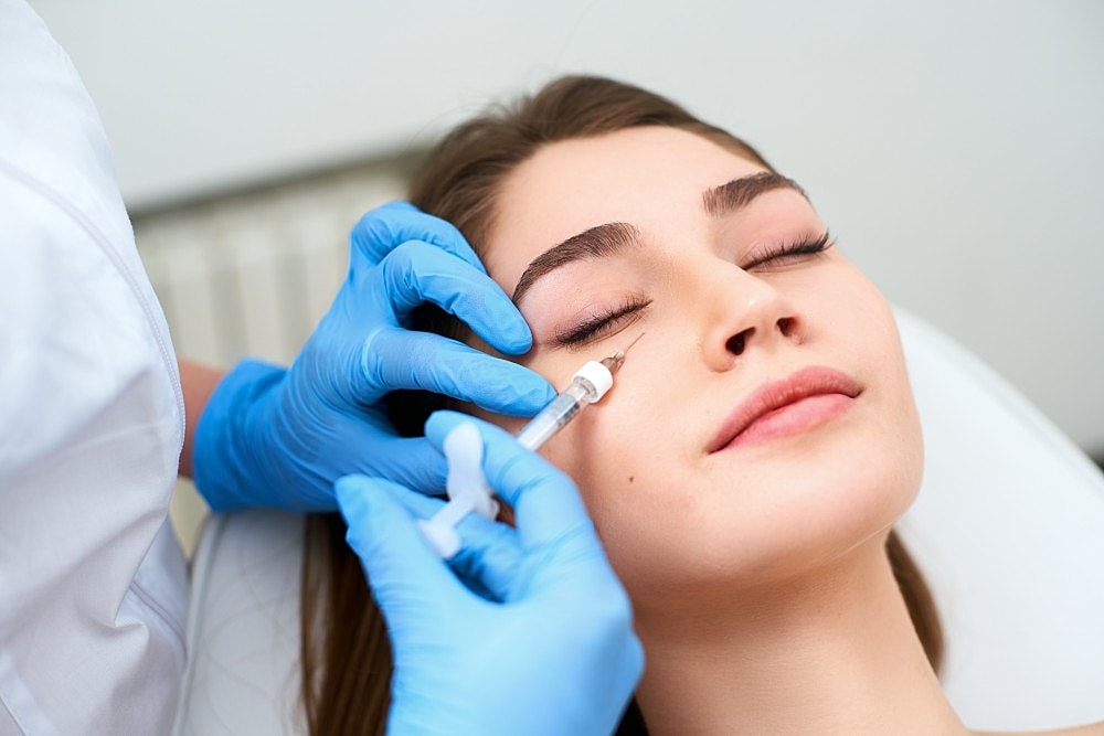 Woman receiving under-eye dermal fillers at a clinic.