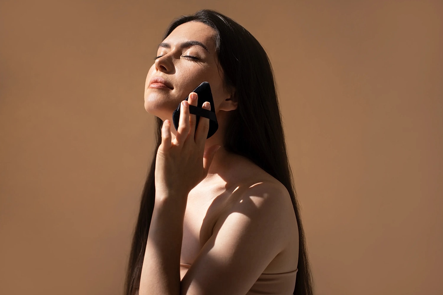 Person gently presses a skincare applicator against the jawline with eyes closed.