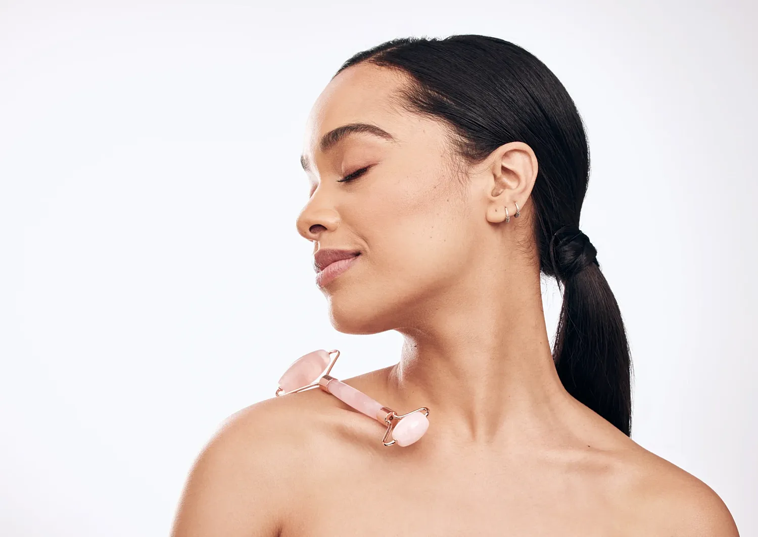 Woman with jade roller on shoulder, serene expression.