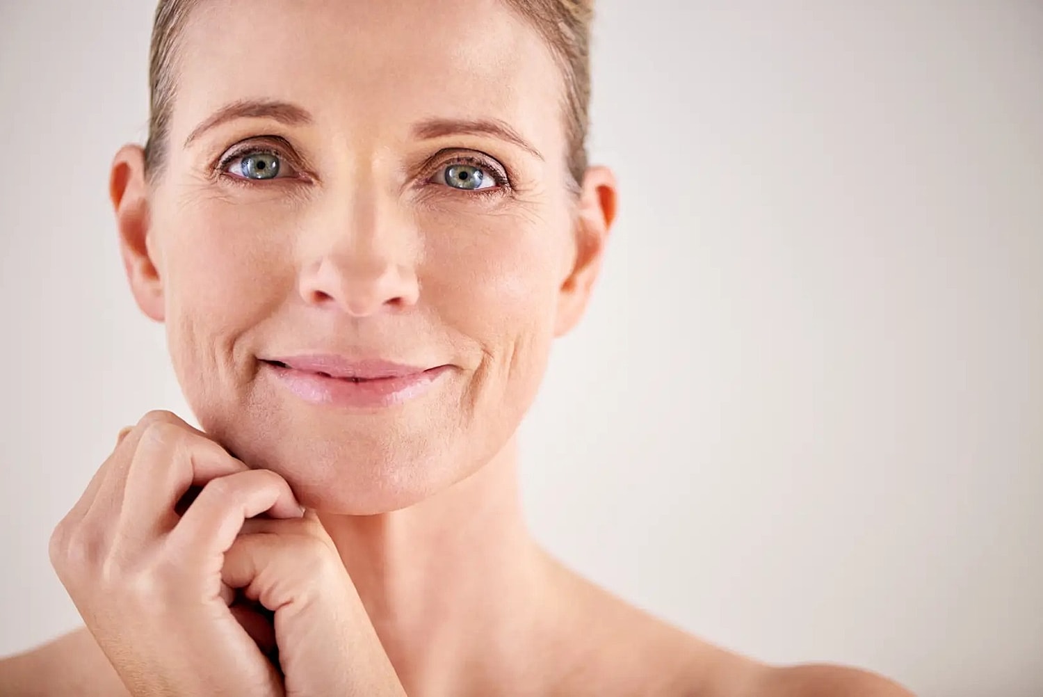 Mature woman with short hair looking at the camera with her hands resting beneath her chin.
