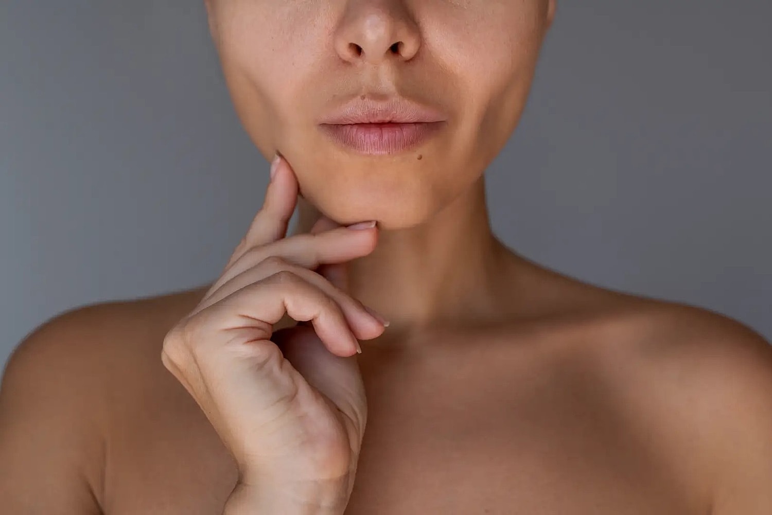 Close-up of a woman's lower face with her fingers resting along her chin and jawline.