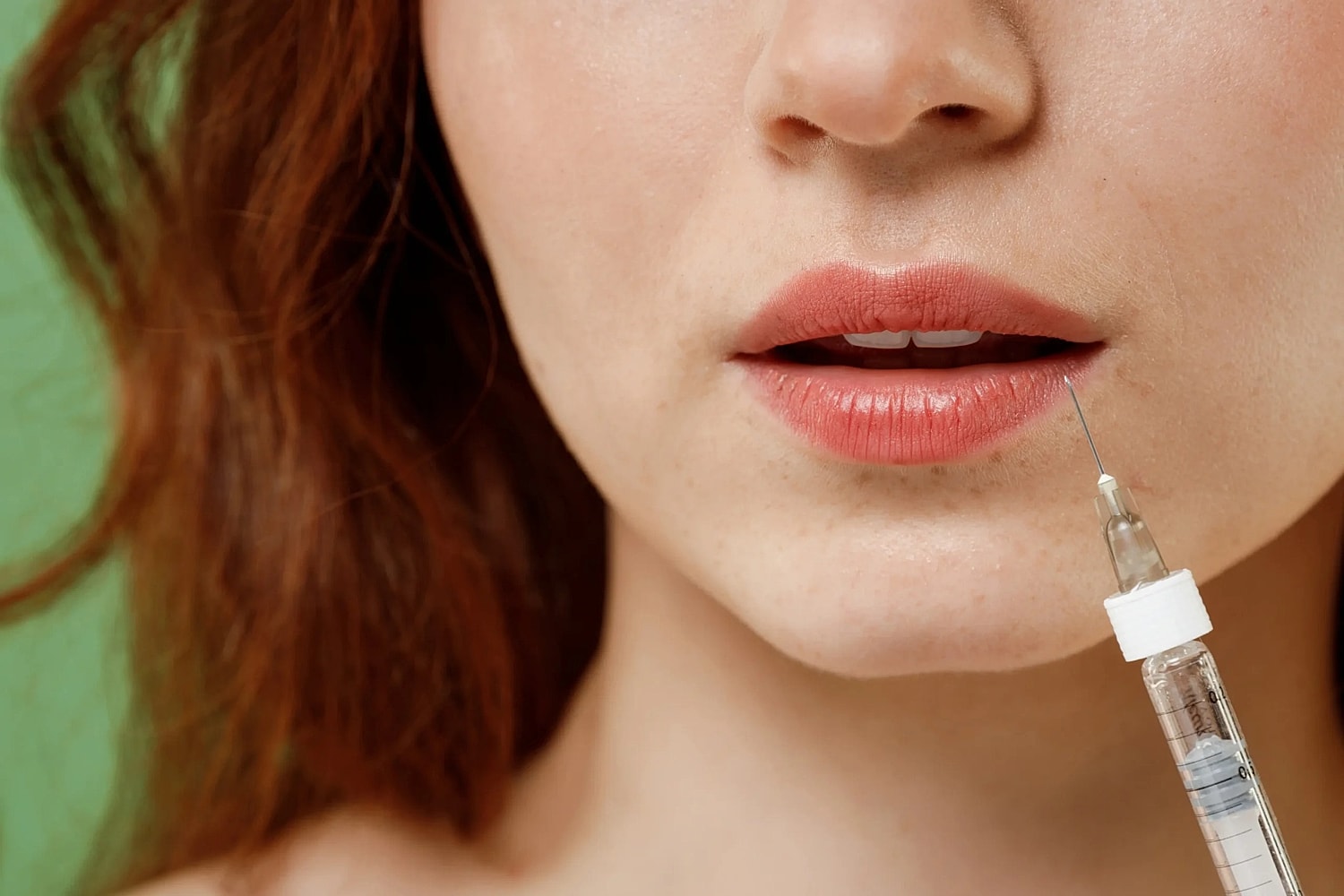Close-up of a woman's lips with a syringe needle positioned near the corner of her lower lip.