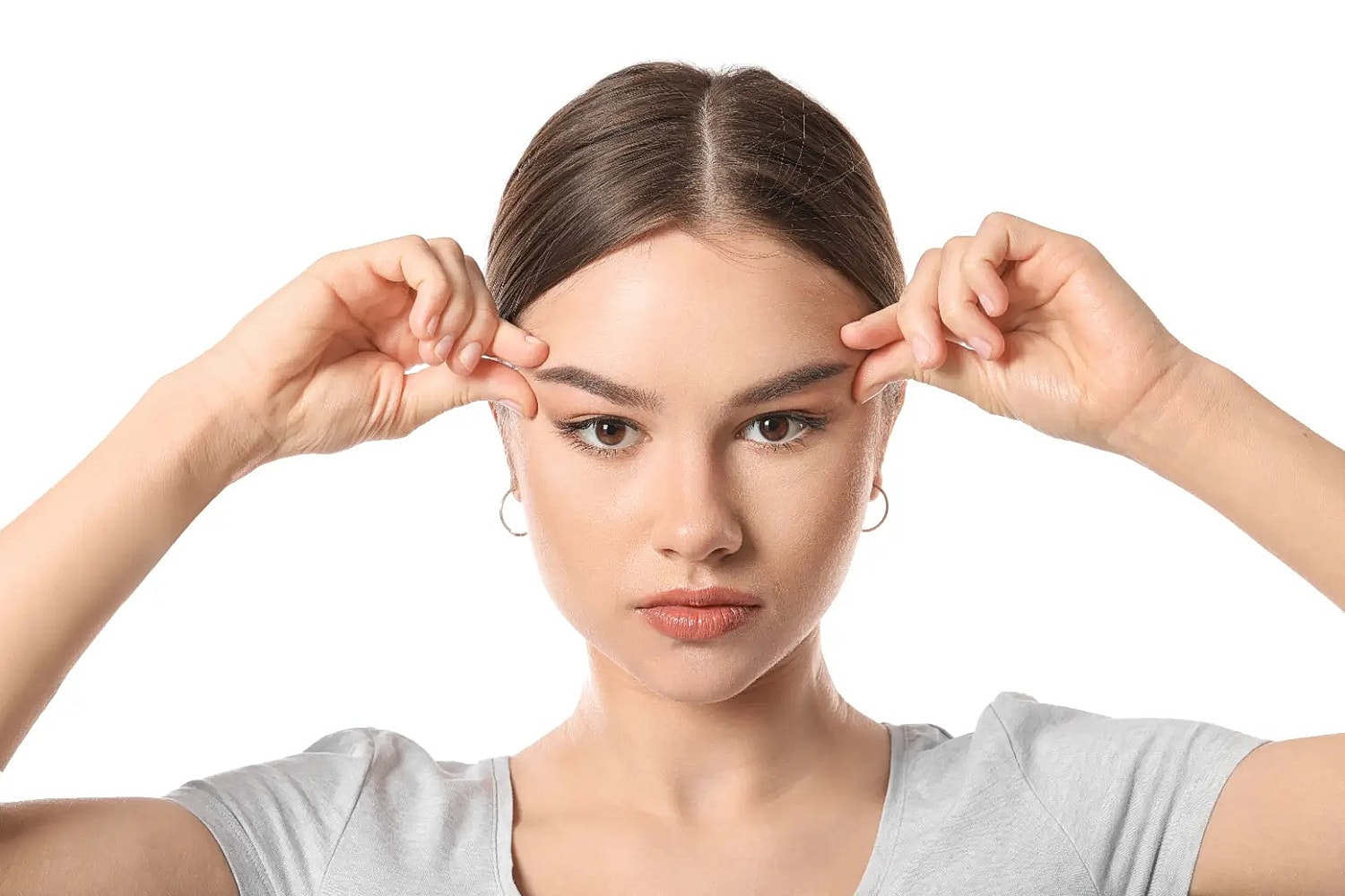 Woman pulling the skin near her eyebrows upward against a light background