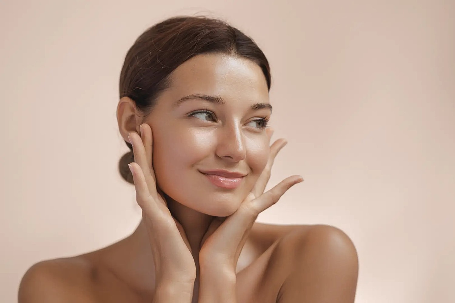 Woman touching her face with both hands against a beige background