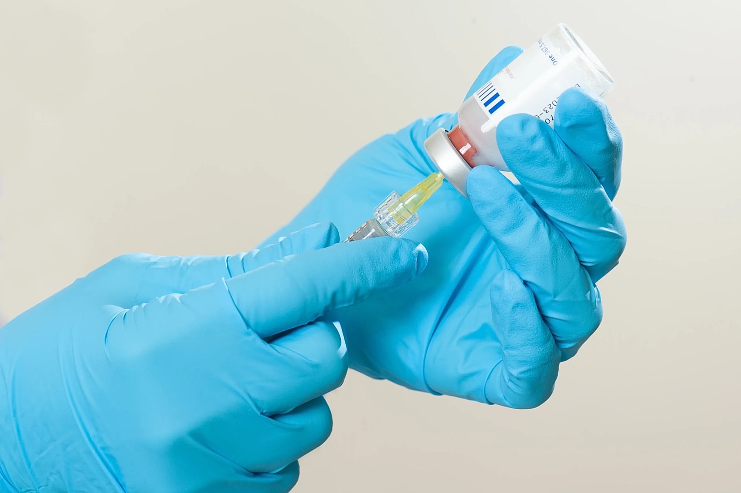 Gloved hands drawing solution from a vial into a syringe