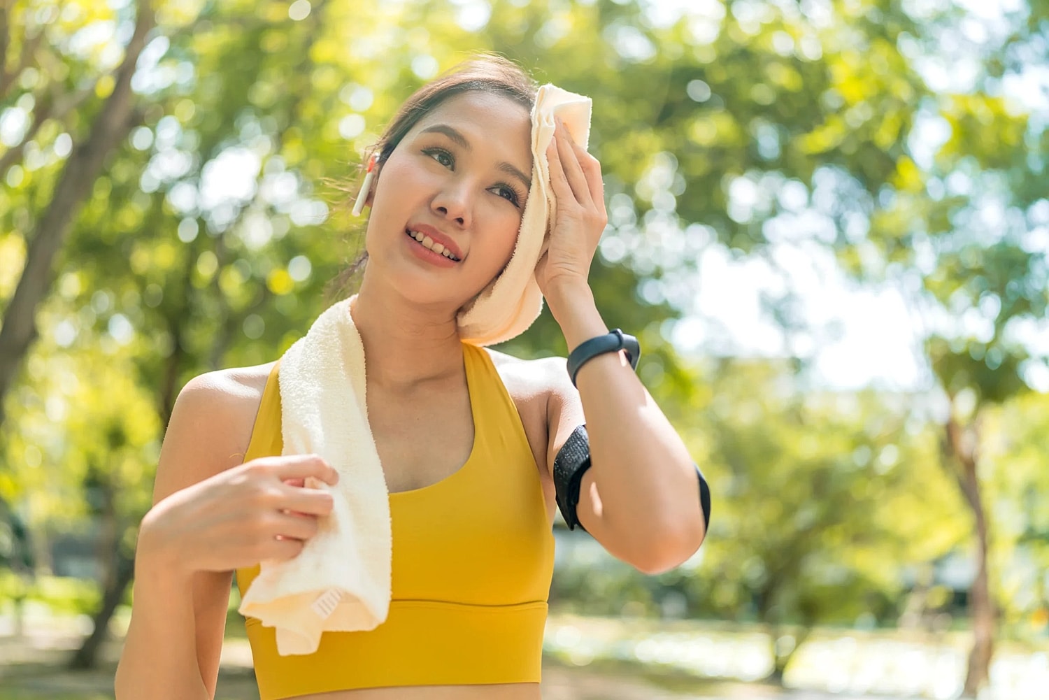 Woman in a yellow athletic top wiping sweat from her face with a towel outdoors