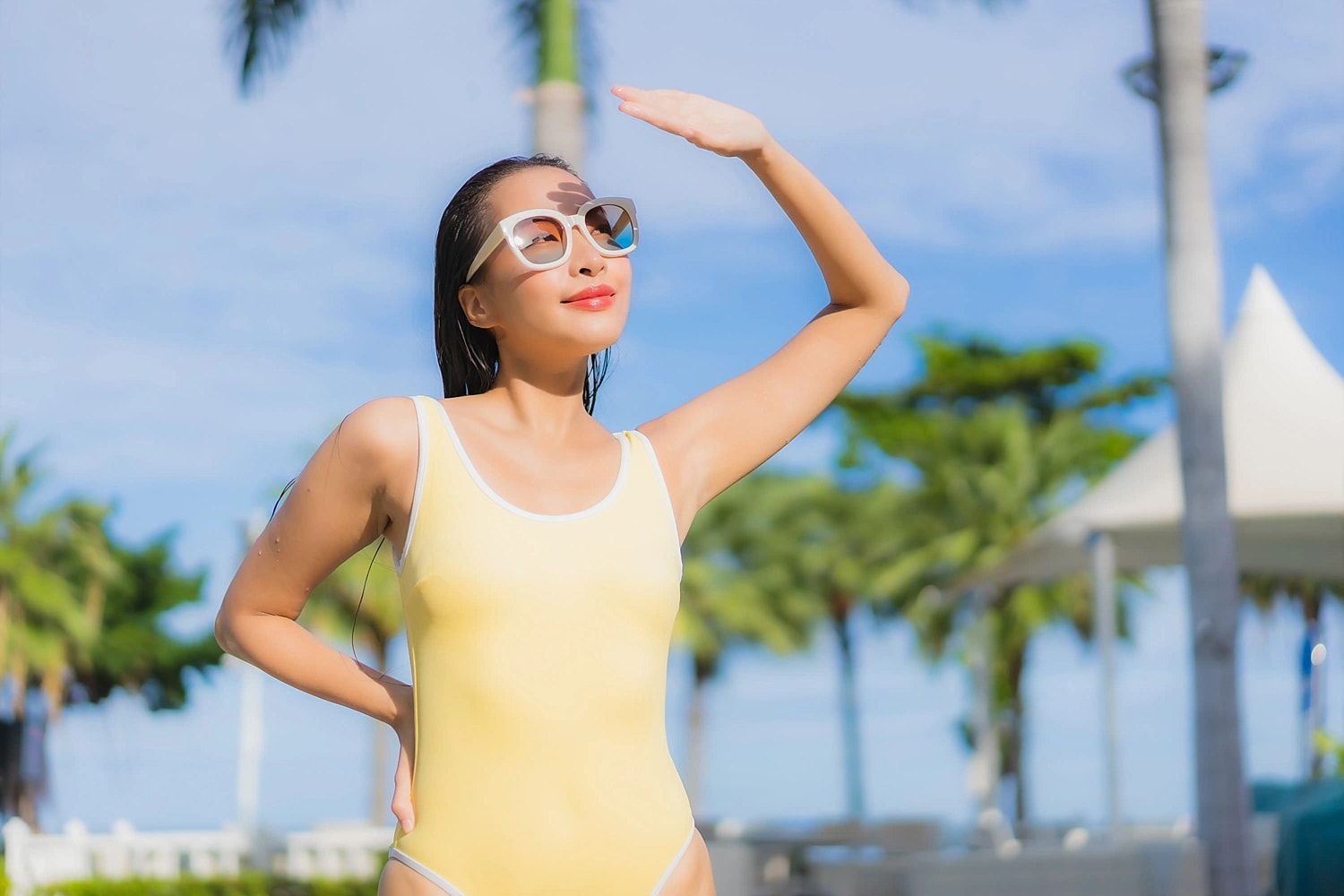Woman in sunglasses shielding her eyes from sunlight near an outdoor pool area