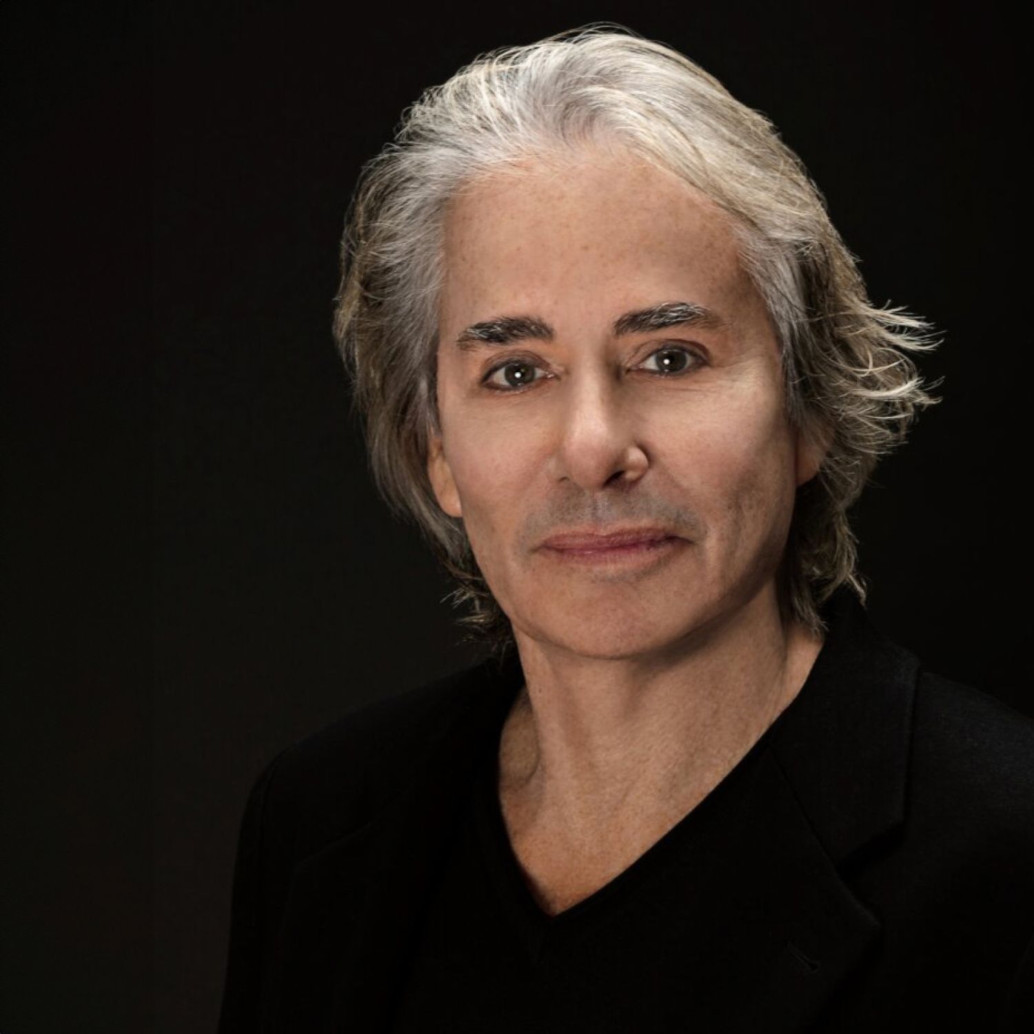 Man with silver hair against a dark background.