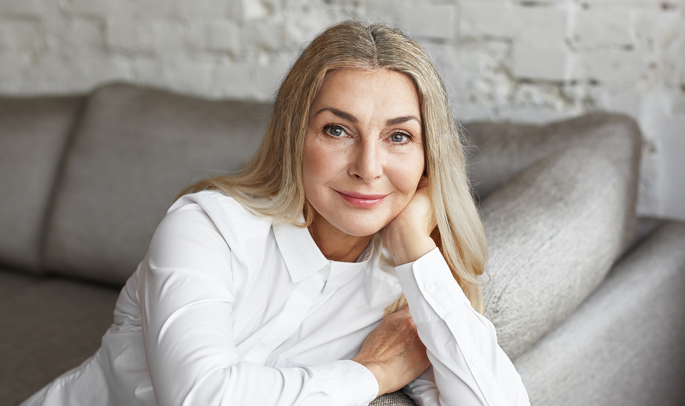 Smiling woman with long, blonde hair sitting indoors.
