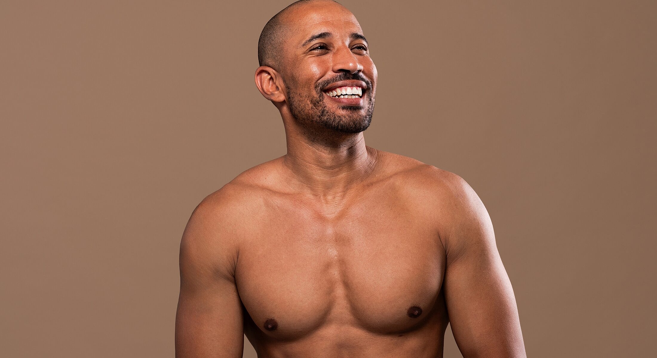 Smiling man with a muscular physique against brown background