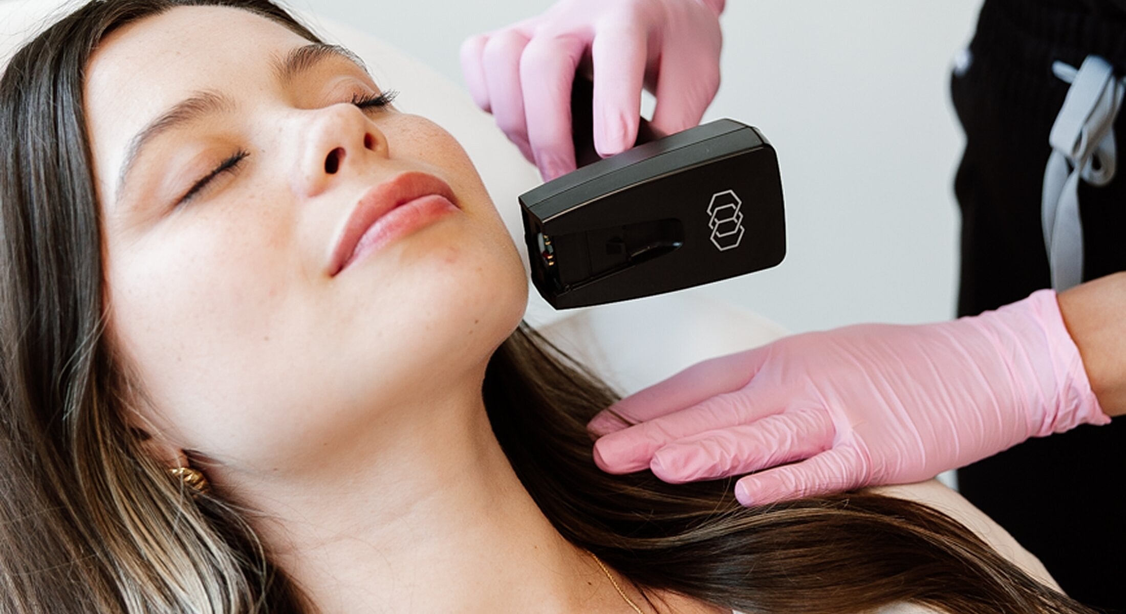 Facial treatment with handheld device and pink gloves.