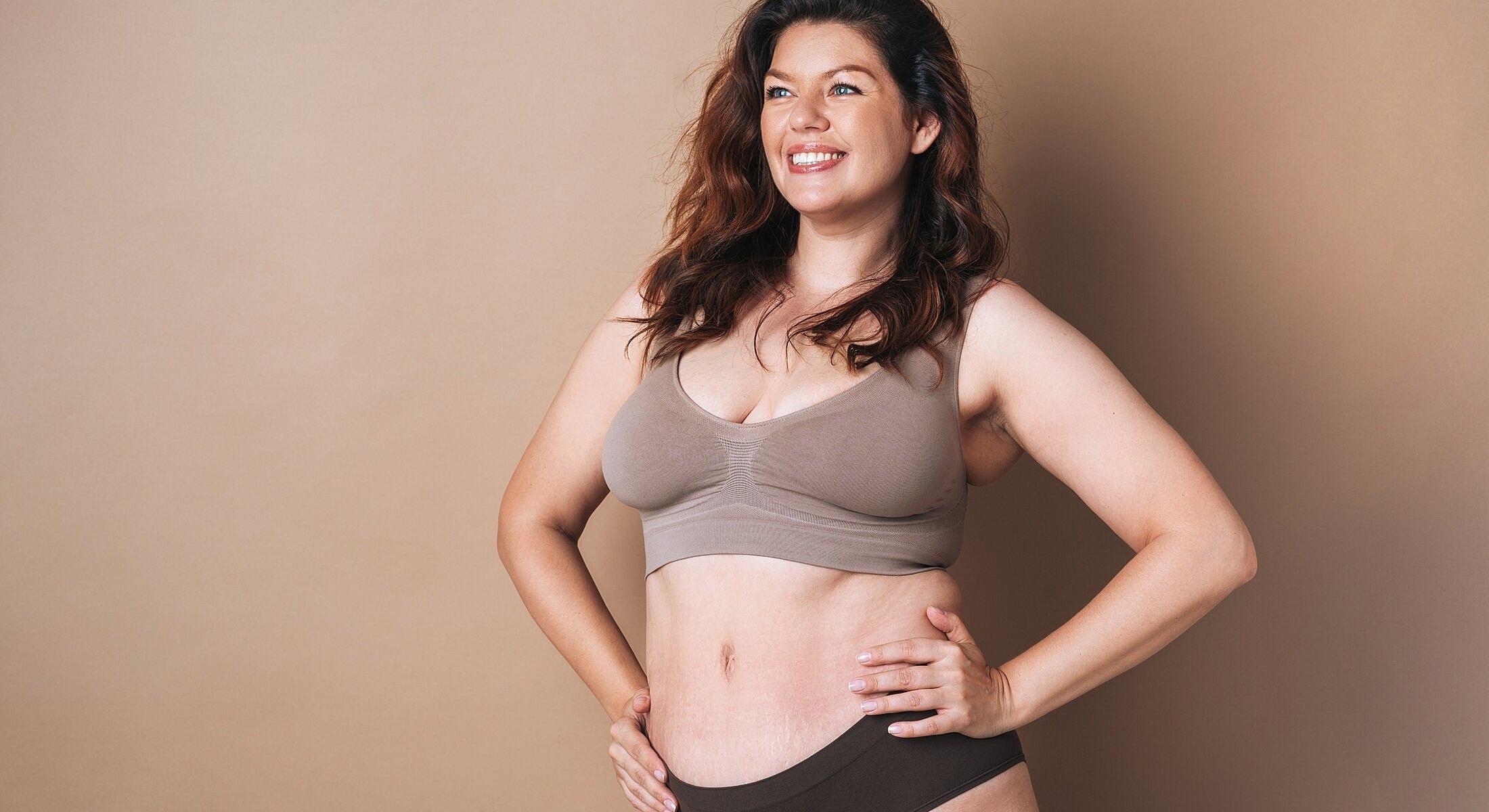 Smiling woman in neutral lingerie against beige background.