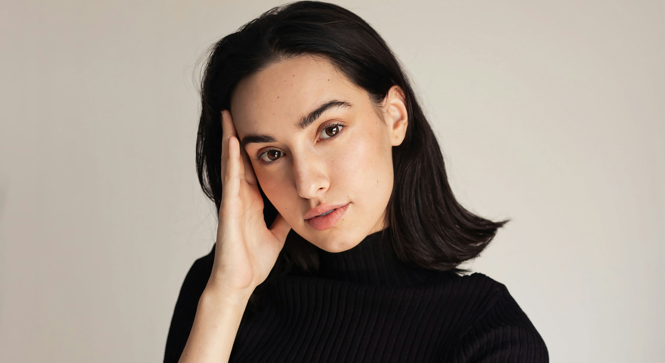 Woman with hand on face against plain background.