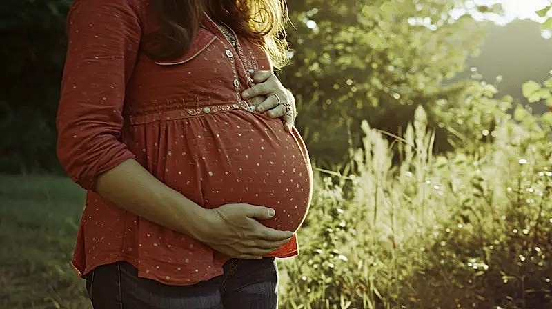Pregnant woman gently holding her belly outdoors.