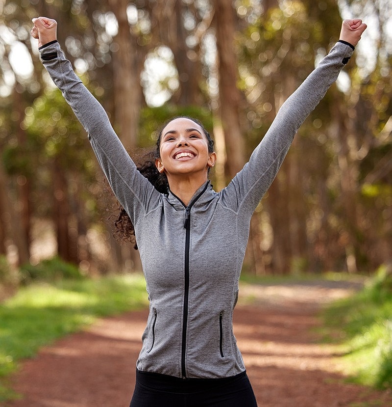 Woman joyfully celebrating outdoors with raised arms.