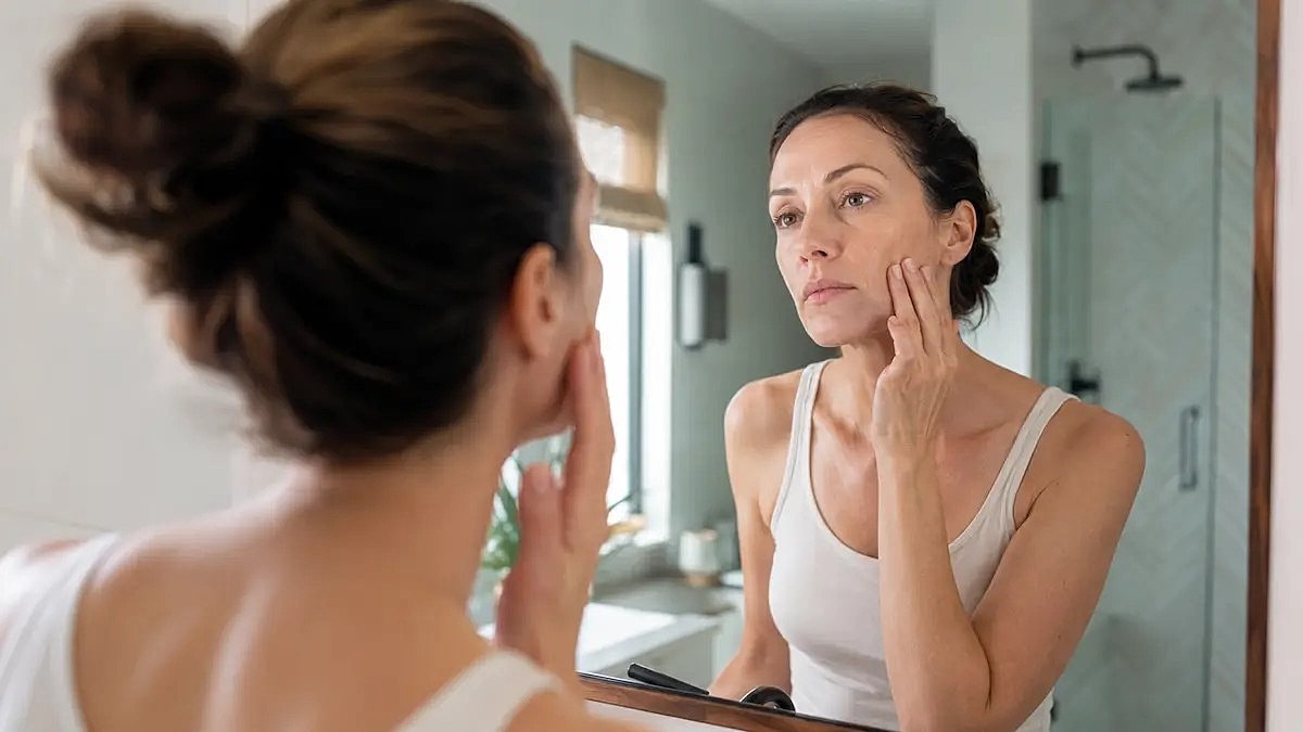 Woman assessing her skin in bathroom mirror.