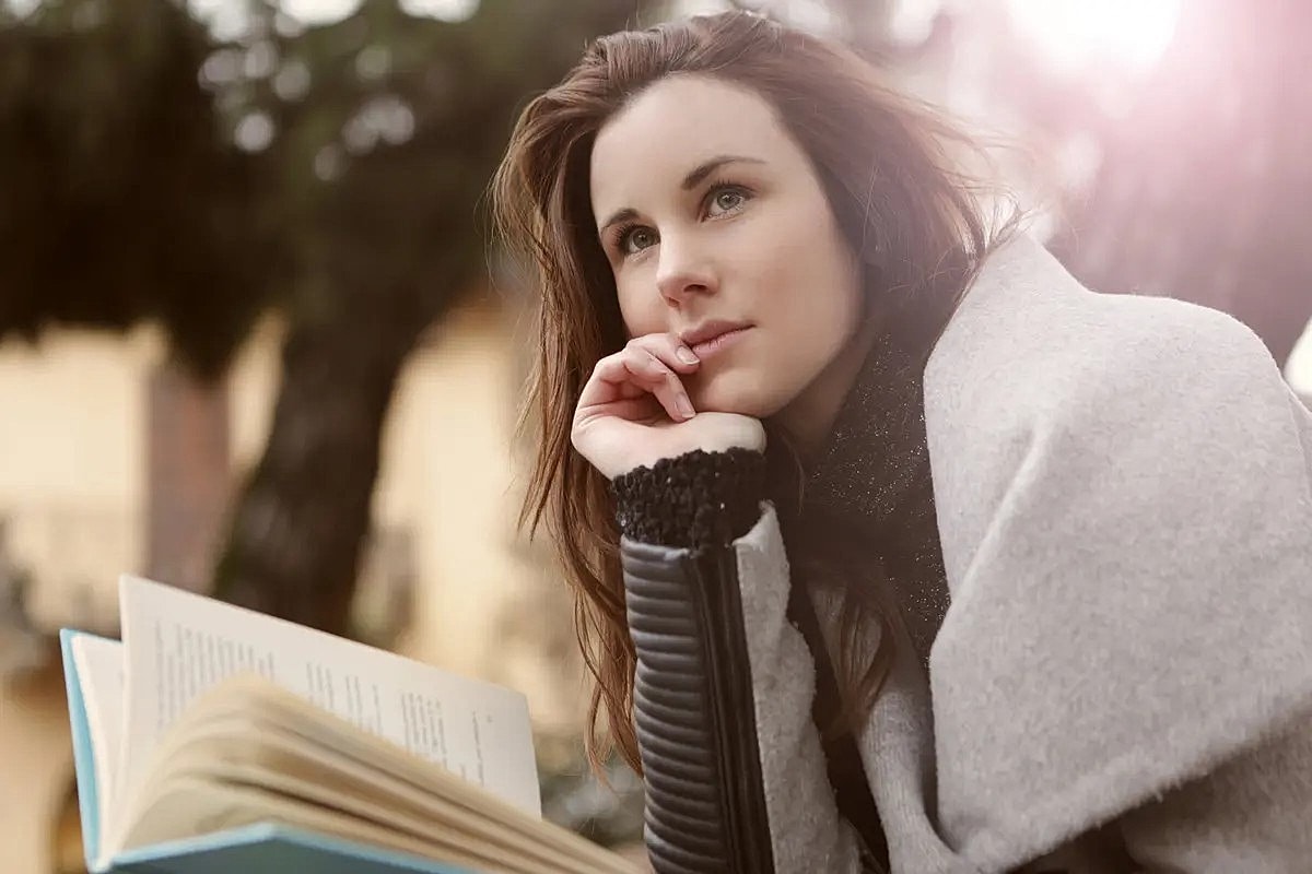 Woman reading a book outdoors, deep in thought.