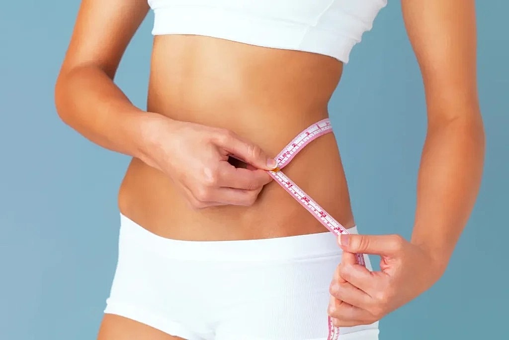 Woman measuring waist with tape measure.