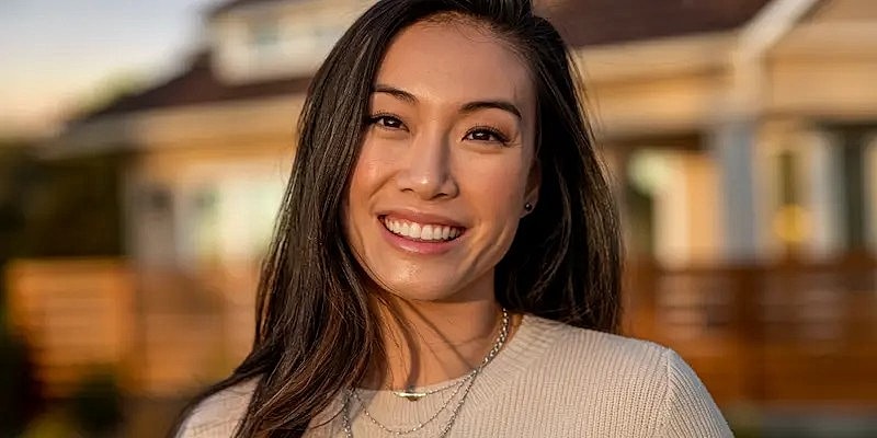 Smiling woman outdoors, wearing light sweater.