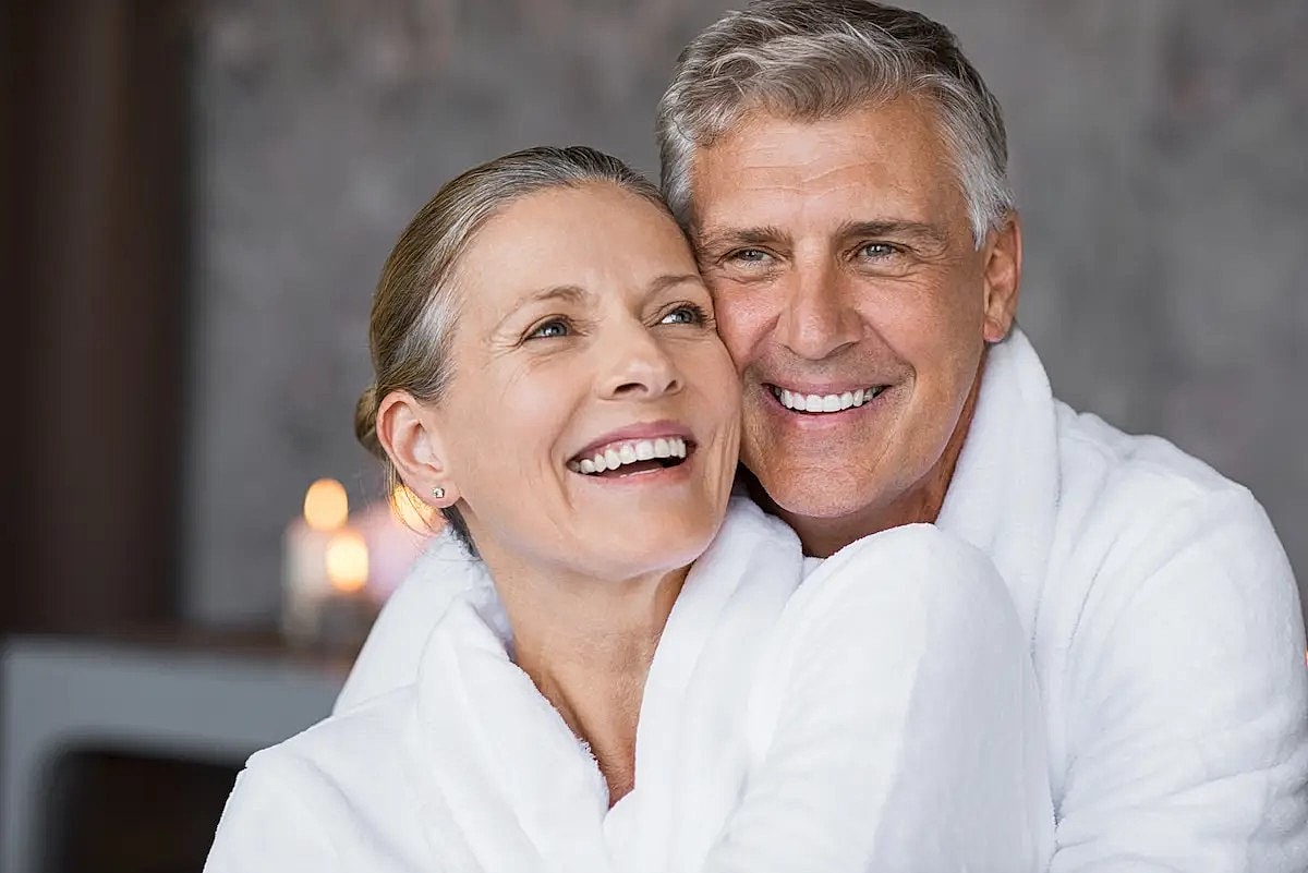 Smiling couple in white robes, cozy atmosphere.