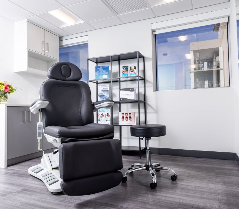 Modern medical examination room with chair and tools.
