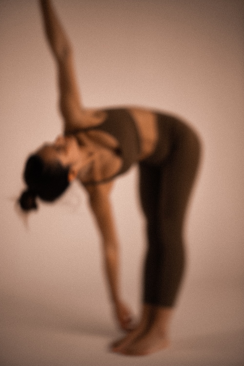 Soft-focus portrait of a woman in a backbend yoga pose against a warm neutral background.