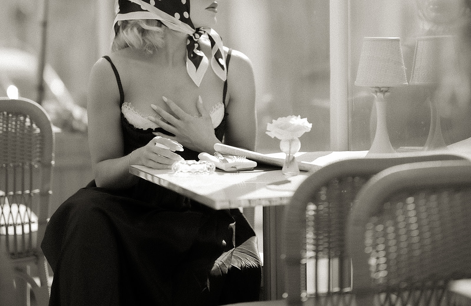 Black-and-white café portrait with a silk scarf, an open neckline and natural window light
