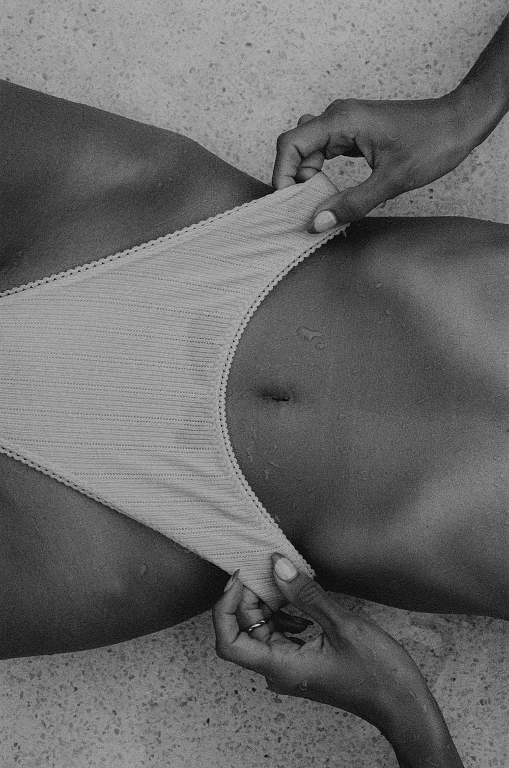 Black-and-white editorial crop of an abdomen beside white swimwear